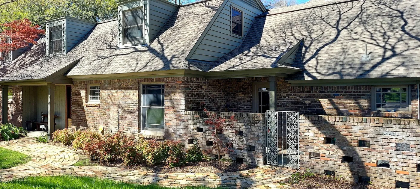 A brick Cape Cod with three dormers and a weathered grey shingle roof