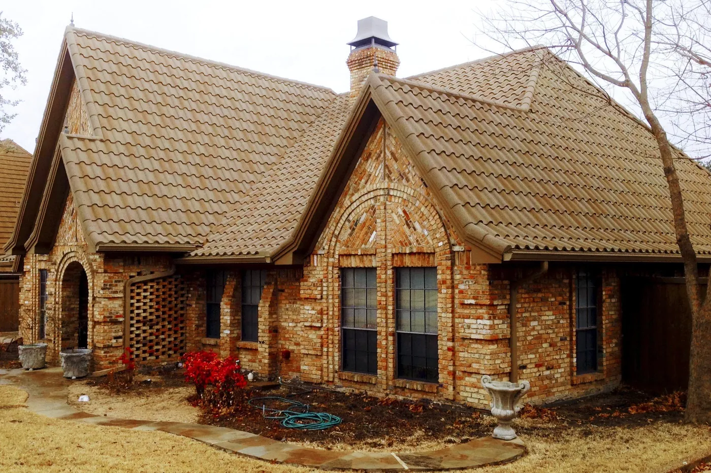 A brick cottage with an arched entry and a tan stone-coated steel tile roof
