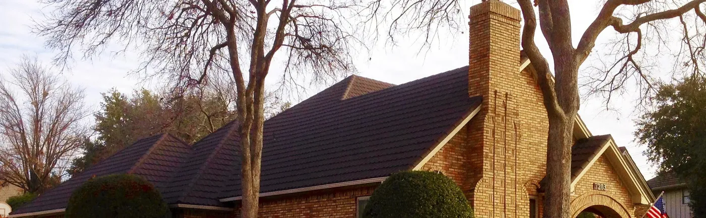 A brick home with a stone chimney and a dark stone-coated steel roof