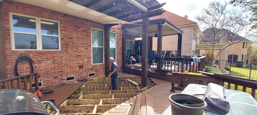 A new deck being framed under a pergola behind a brick home