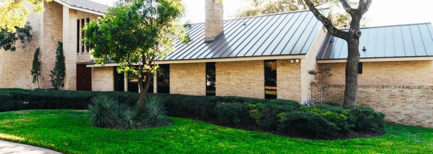 A tan brick home with a grey standing seam metal roof
