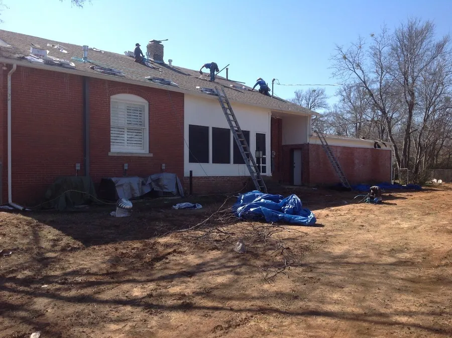 Three crew members re-roofing the back of a brick two-story
