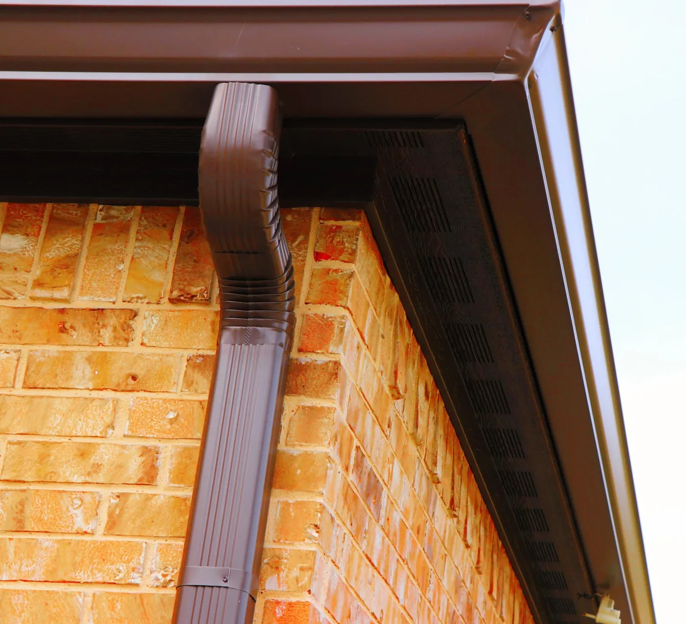 Looking up at a brown seamless gutter corner and downspout
