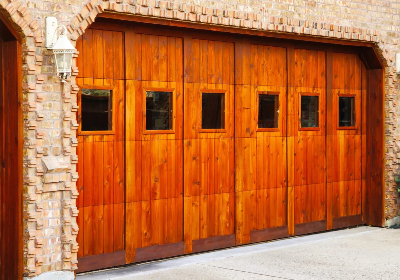 A cedar-stained garage door with a row of windows in an arched brick opening