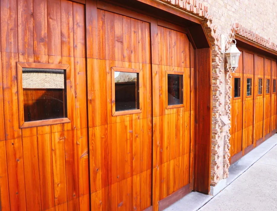 Cedar-stained garage doors with windows along a brick wall