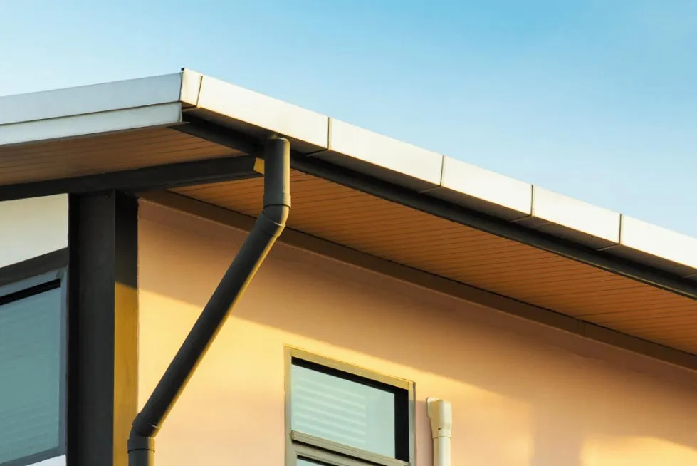 A white box gutter and black downspout on a commercial building