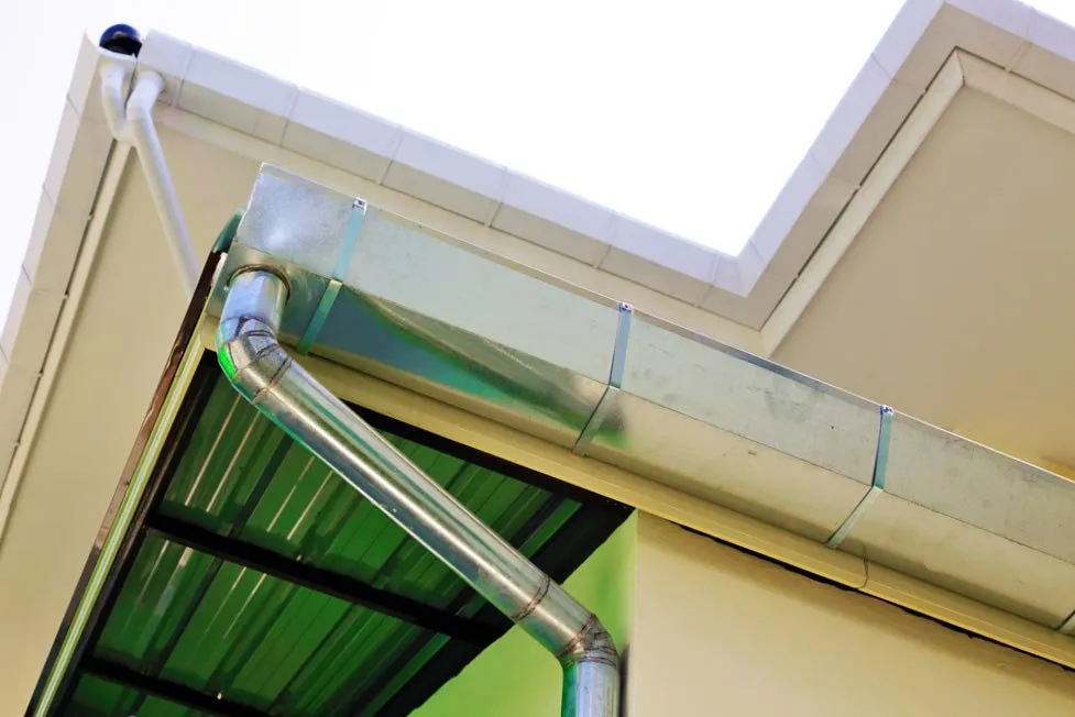 A commercial box gutter and galvanized downspout under a metal canopy