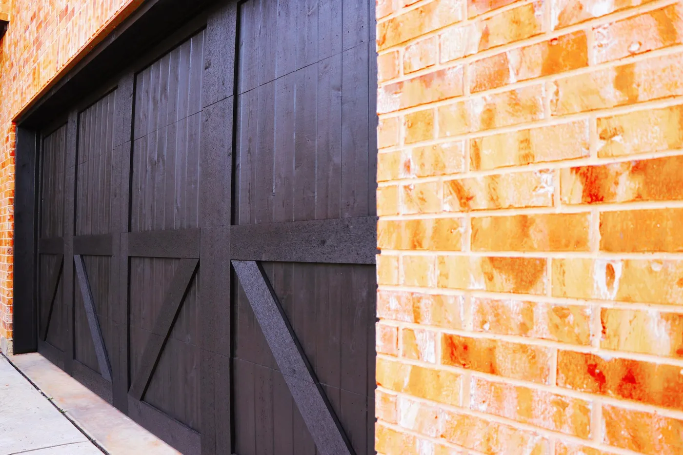A dark-stained carriage garage door beside tan brick