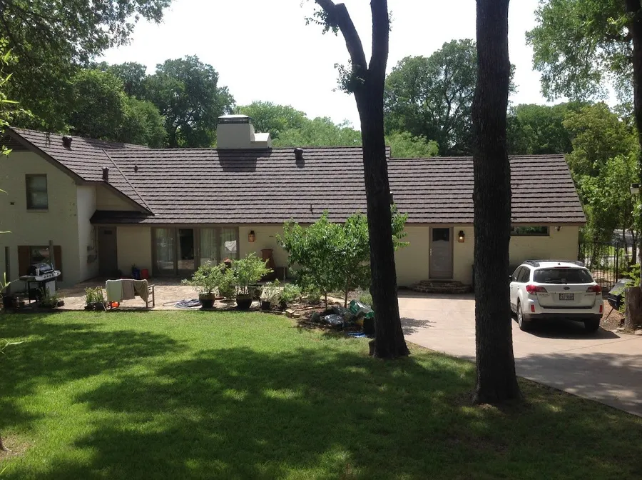 A long one-story home with a brown stone-coated steel shake roof under shade trees