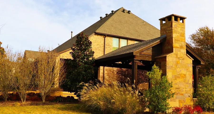 A brick two-story with a stone chimney, a timber pergola and a dark shingle roof