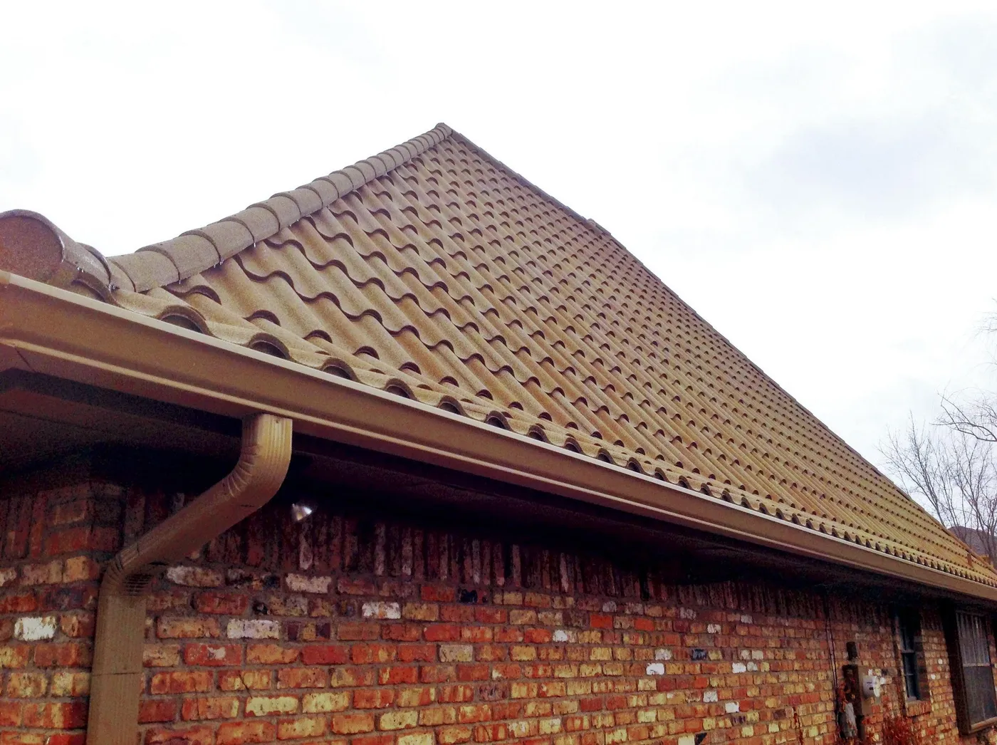 The edge of a stone-coated steel tile roof with a matching gutter