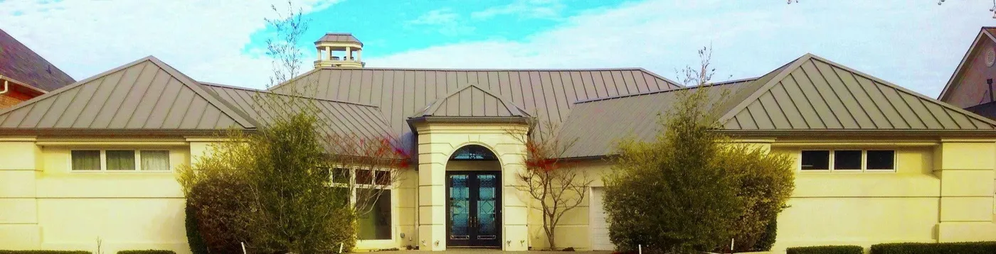 A cream stucco home with a bronze standing seam metal roof