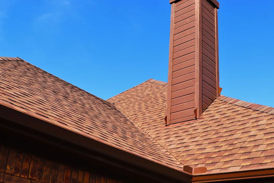 A terracotta-red shingle roof and a metal-clad chimney against a blue sky