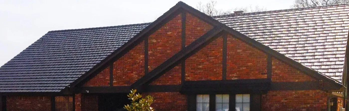 A Tudor brick gable under a charcoal metal shingle roof