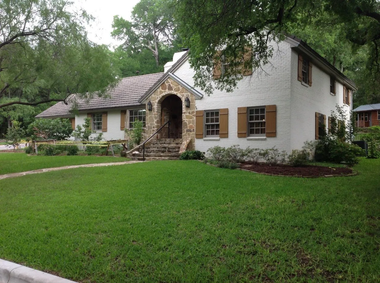 A painted white brick two-story with a stone arched entry and a shingle roof